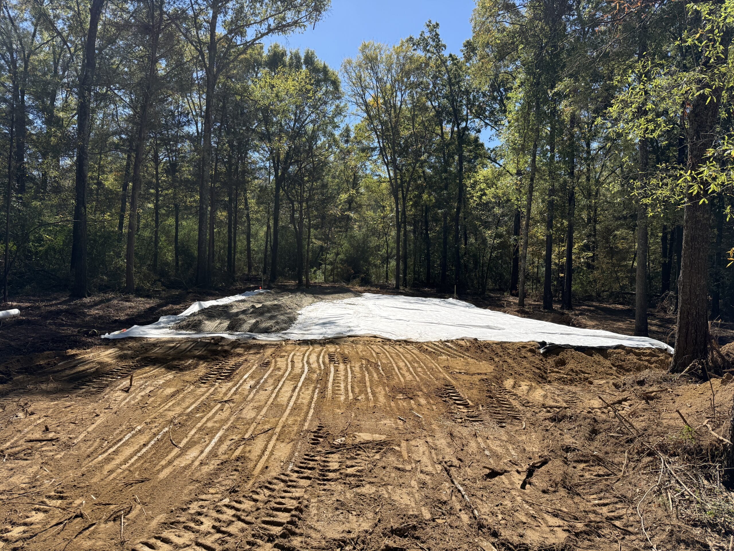 Geotextile fabric covering sand base in cleared forest area.